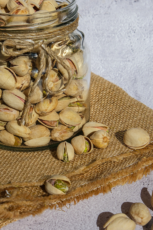Pistachios in glass jar on concrete background. Organic pistachios, healthy food. Heap or stack of pistachios. Vegan omega nutrition. Roasted salted pistachios.