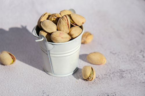 Pistachios in white bucket on concrete background. Healthy and dietary nutrition. Concept of nuts. Vegan protein omega vitamin food. Roasted salty pistachio. Harvest