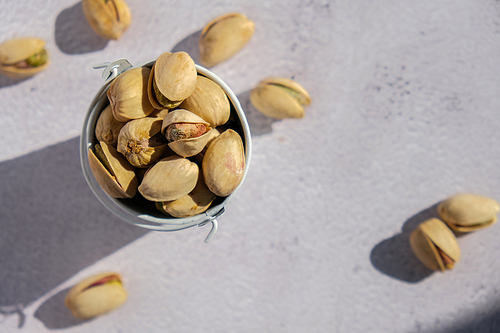 Pistachios in white bucket on concrete background. Healthy and dietary nutrition. Concept of nuts. Vegan protein omega vitamin food. Roasted salty pistachio. Harvest