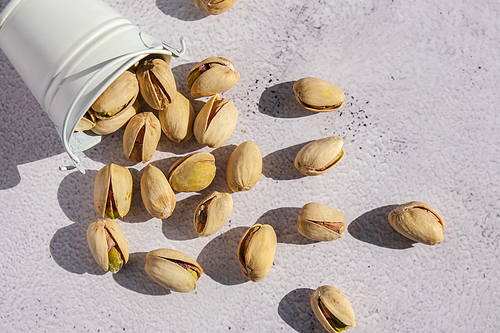 Pistachios in white bucket on concrete background. Healthy and dietary nutrition. Concept of nuts. Vegan protein omega vitamin food. Roasted salty pistachio. Harvest
