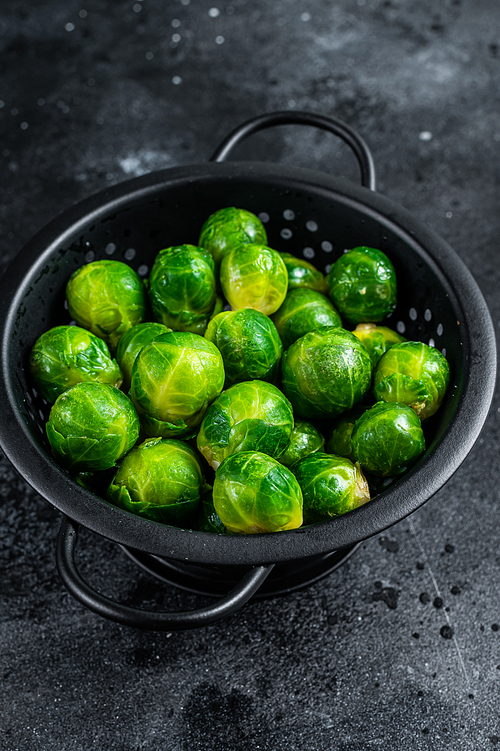Brussels sprouts green cabbage in colander. Black background. Top view.