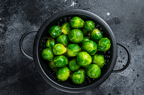 Brussels sprouts green cabbage in colander. Black background. Top view.
