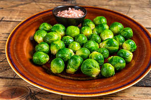 Cooked Brussels green sprouts cabbage in a rustic plate with salt. wooden background. Top view.