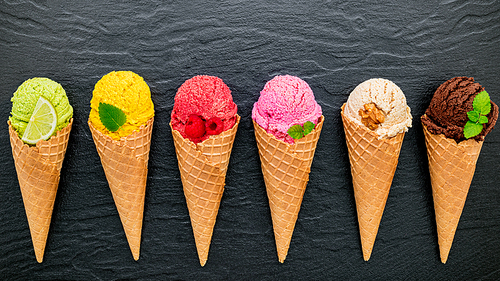 Various of ice cream flavor in cones blueberry ,lime ,pistachio ,almond ,orange ,chocolate ,vanilla and coffee set up on dark stone background . Summer and Sweet menu concept.