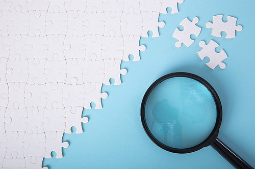 Set of puzzle pieces with magnifying glass background. Detective research concept