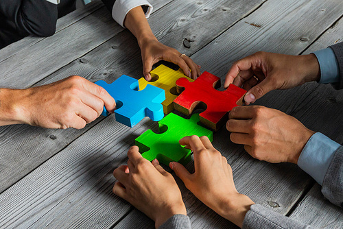 Business people team sitting around meeting table and assembling color jigsaw puzzle pieces unity cooperation ideas concept