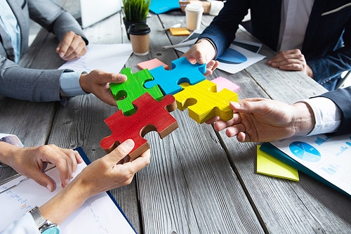 Business people team sitting around meeting table and assembling color jigsaw puzzle pieces unity cooperation ideas concept