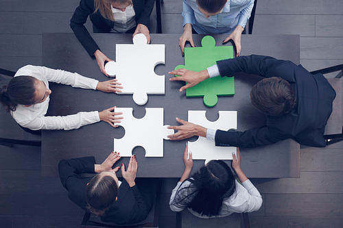 Group of business people assembling jigsaw puzzle at office table, top view, team support and help concept, green and white pieces