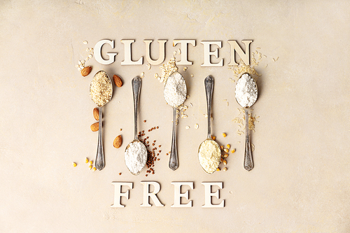 metal spoons of various gluten free flour almond flour, oatmeal flour, buckwheat flour, ., corn flour and gluten free lettering made of wooden letters