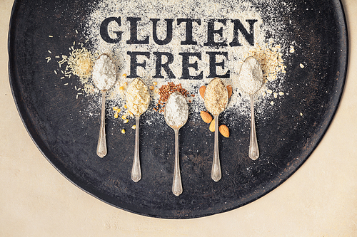 gluten free written in flour on vintage baking sheet and spoons of various gluten free flour (almond flour, buckwheat flour, ., corn flour, oatmeal flour), gluten free baking concept