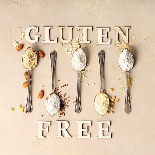 metal spoons of various gluten free flour (almond flour, oatmeal flour, buckwheat flour, ., corn flour) and gluten free lettering made of wooden letters