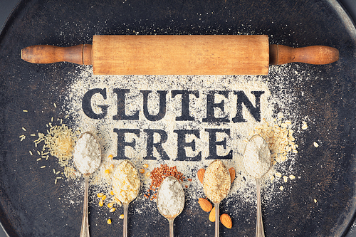 gluten free written in flour on vintage baking sheet, rolling pin and spoons of various gluten free flour (almond flour, buckwheat flour, ., corn flour, oatmeal flour), gluten free baking concept