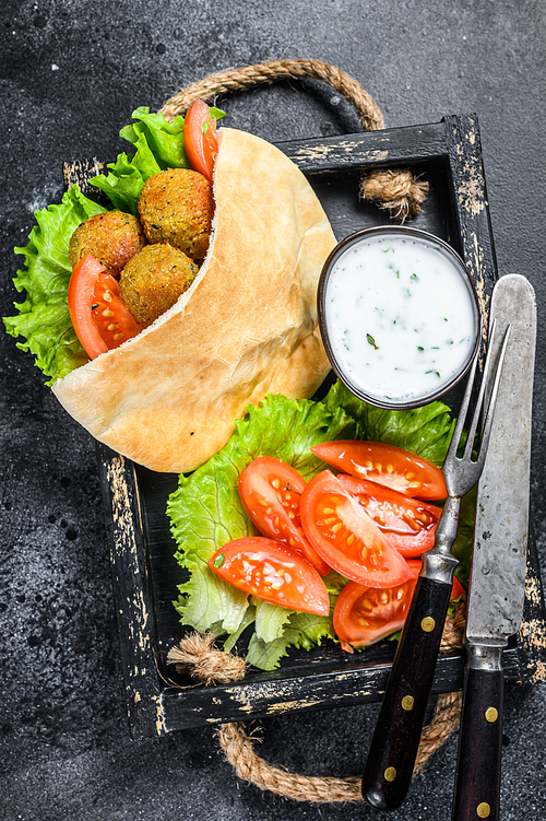 Falafel with vegetables, sauce in pita bread, vegetarian kebab sandwich. Black background. Top view.