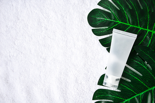 Mockup empty Facial skincare organic natural product white tube on soft crumpled white cloth decoration with blurred monstera deliciosa. Beauty product with spf factor. Copy space
