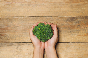 Fresh broccoli in hands on a wooden background