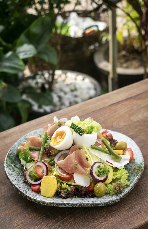 nicoise style healthy organic rustic salad with egg and ham outdoors