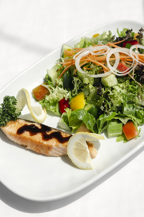 organic mixed vegetable salad with salmon fillet and balsamic vinaigrette on white restaurant table