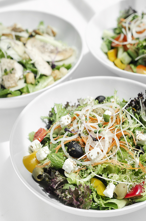 mixed fresh organic salads in bowls on white restaurant table