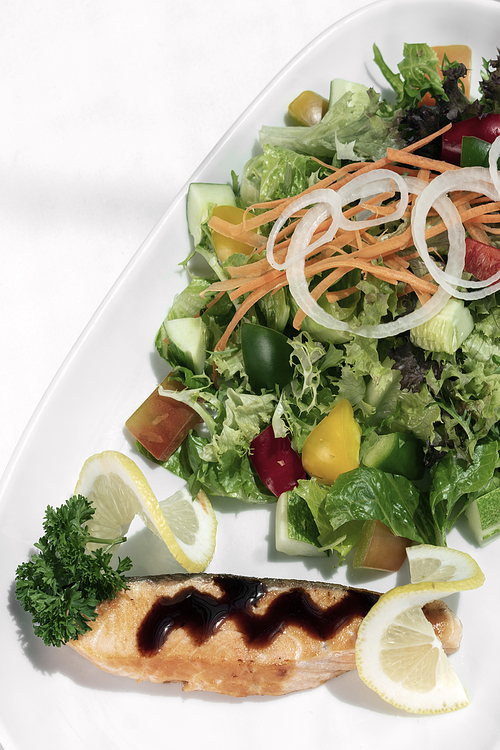 organic mixed vegetable salad with salmon fillet and balsamic vinaigrette on white restaurant table