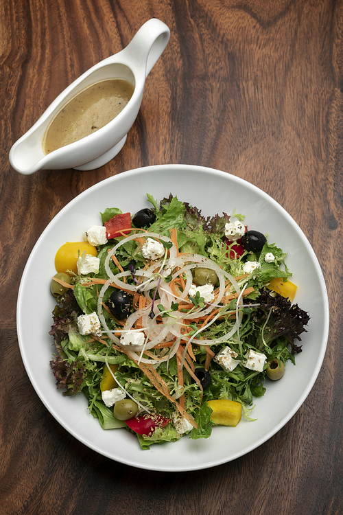 greek salad with feta cheese and olives with citrus vinaigrette on wooden table