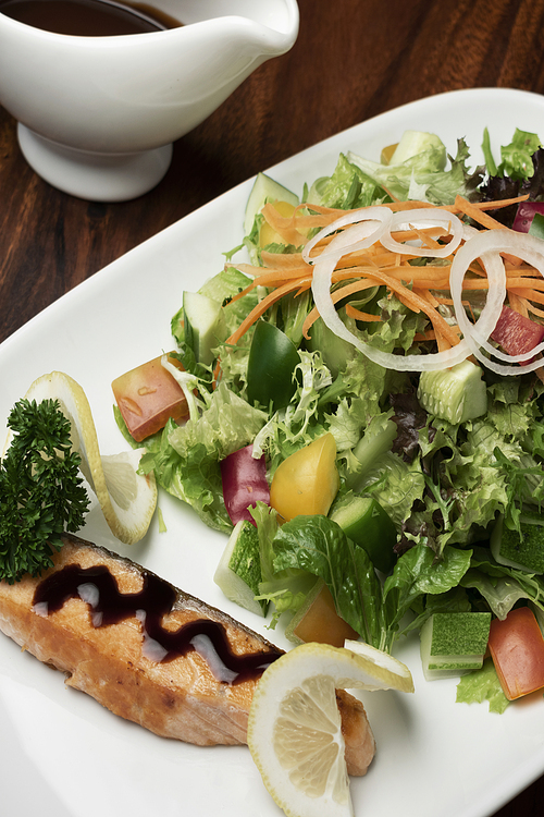 organic mixed vegetable salad with salmon fillet and balsamic vinaigrette on wood restaurant table