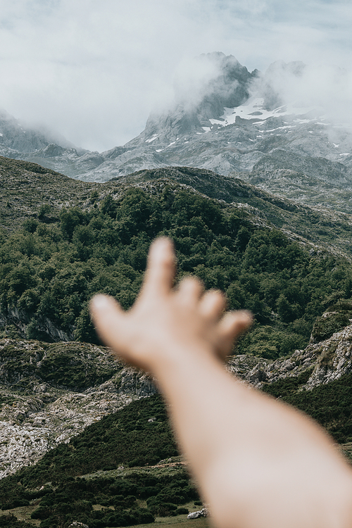 Moody wallpaper of an out of focus hand in front of a colorful landscape of the mountains of Asturias during a sunny day, Covadonga lakes, peaceful scenario, snowy mountains, copy space