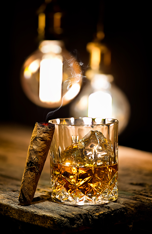 Cigar and glass with whiskey with ice cubes