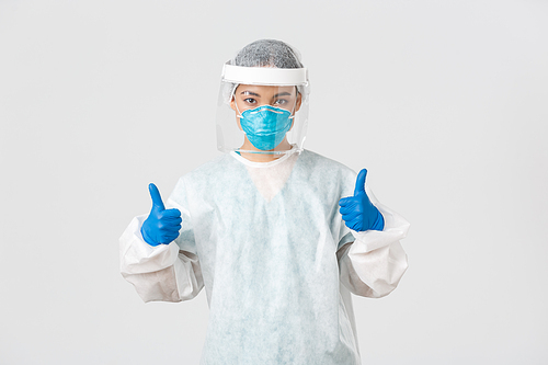 Covid-19, coronavirus disease, healthcare workers concept. Confident serious-looking asian female doctor working in contagious zones in personal protective equipment, show thumbs-up.