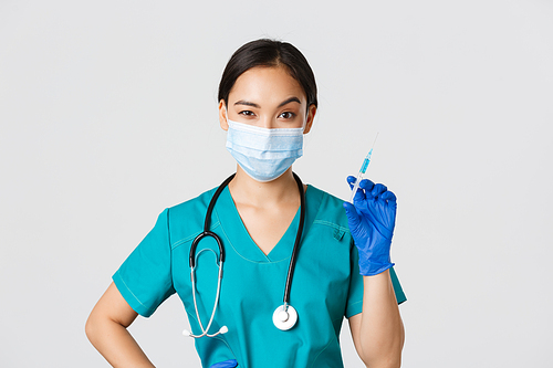 Covid-19, coronavirus disease, healthcare workers concept. Sassy cute asian female nurse, intern in medical mask and gloves holding syringe with vaccine, ready to make shot, white background.