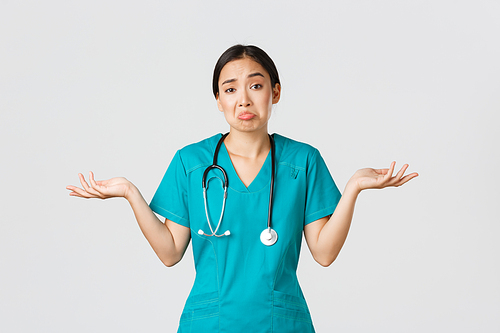 Covid-19, healthcare workers, pandemic concept. Portrait of clueless asian female nurse, woman doctor shrugging and spread hands sideways unaware, dont know, cant help, white background.