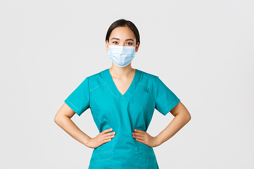 Covid-19, coronavirus disease, healthcare workers concept. Cheerful smiling asian female doctor, physician in scrubs and medical mask, looking upbeat, working with patients in hospital.