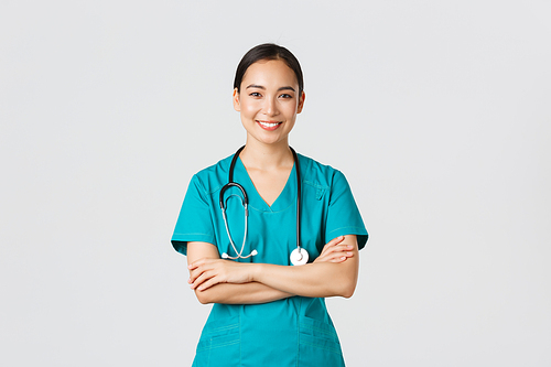 Covid-19, healthcare workers, pandemic concept. Portrait of confident smiling, attractive asian female nurse in scrubs, with stethoscope, cross arms chest and looking at camera, white background.