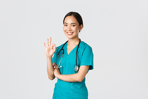 Covid-19, healthcare workers, pandemic concept. Confident professional asian doctor, female physician in scrubs, showing okay gesture, guarantee quality of services in hospital, approve and agree.