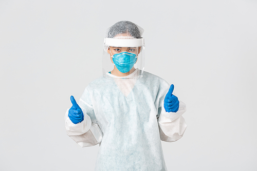 Covid-19, coronavirus disease, healthcare workers concept. Serious-looking confident young asian female doctor, infectionist in personal protective equipment showing thumbs-up, enter dangerious zone.