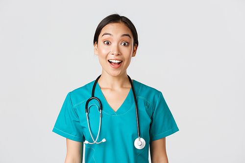 Healthcare workers, preventing virus, quarantine campaign concept. Happy and excited asian female doctor, physician in scrubs look amazed, hear awesome news, white background.