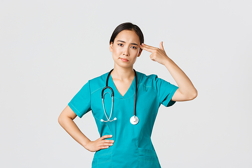 Covid-19, healthcare workers, pandemic concept. Exhausted and bothered, annoyed asian female doctor, nurse making shot gun gesture over head from boredom, white background.