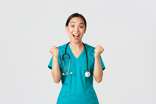 Covid-19, healthcare workers and preventing virus concept. Hopeful and relieved, joyful asian pretty female doctor, physician rejoicing with fists pump, congrats or praise someone, winning.