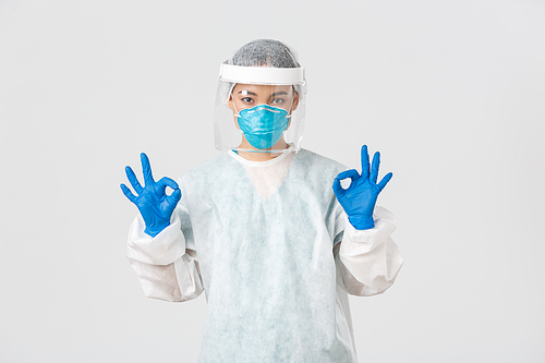 Covid-19, coronavirus disease, healthcare workers concept. Confident and serious asian female doctor, lab technician in personal protective equipment showing okay gesture in approval.