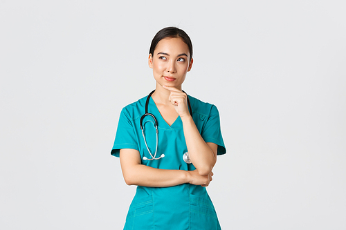 Covid-19, healthcare workers, pandemic concept. Thoughtful smart asian nurse in scrubs looking away and thinking, smiling pleased. Doctor have interesting idea, pondering over white background.
