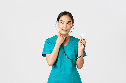 Covid-19, healthcare workers and preventing virus concept. Cute smiling asian female intern learn how listen lungs with stethscope, doctor examine patient, looking thoughtful upper left corner.