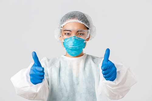 Covid-19, coronavirus disease, healthcare workers concept. Close-up of confident asian female doctor in personal protective equipment showing thumbs-up, recommend or guarantee quality.