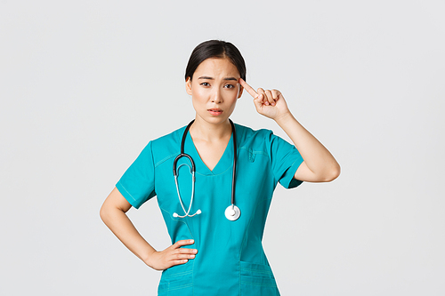 Covid-19, healthcare workers, pandemic concept. Annoyed skeptical asian female nurse or doctor scolding someone acting crazy or stupid, roll finger over temple with judgemental face.