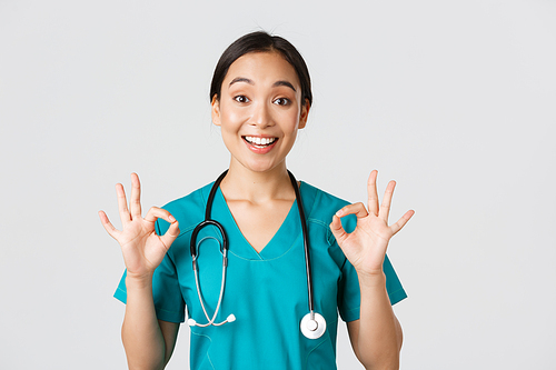 Healthcare workers, preventing virus, quarantine campaign concept. Excited and pleased asian female doctor, nurse in scrubs with stethoscope, showing okay gesture, white background.