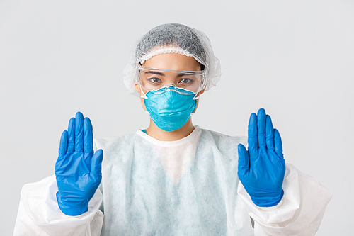 Covid-19, coronavirus disease, healthcare workers concept. Close-up of serious-looking concerned asian female doctor in personal protective equipment show stop gesture, prohibit enter dangerous zone.