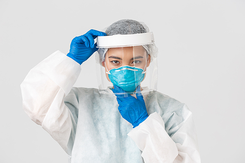 Covid-19, coronavirus disease, healthcare workers concept. Confident serious-looking female asian doctor, put on face shield and respirator, personal protective equipment, white background.