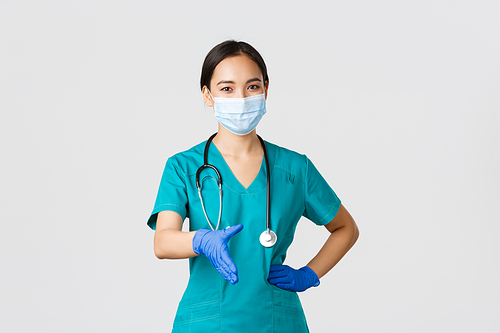 Covid-19, coronavirus disease, healthcare workers concept. Confident young asian female doctor, physician in scrubs and medical mask, gloves, extend hand for handshake, greeting patient.