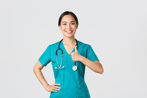 Covid-19, healthcare workers, pandemic concept. Smiling upbeat, confident female asian nurse in scrubs have all under control, show thumbs-up in approval, guarantee quality of service in clinic.