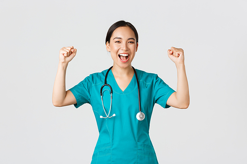 Covid-19, healthcare workers and preventing virus concept. Successful confident asian female doctor or nurse in scrubs fist pump and shouting yes, rejoicing, encourage herself, aim for victory.