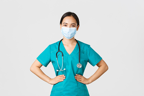 Covid-19, coronavirus disease, healthcare workers concept. Confident professional physician, doctor in medical mask and scrubs working her shift clinic, looking determined, white background.
