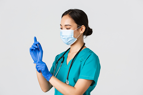 Covid-19, coronavirus disease, healthcare workers concept. Professional smiling asian female nurse, physician in scrubs and medical mask put on rubber gloves for checkup, patient examination.